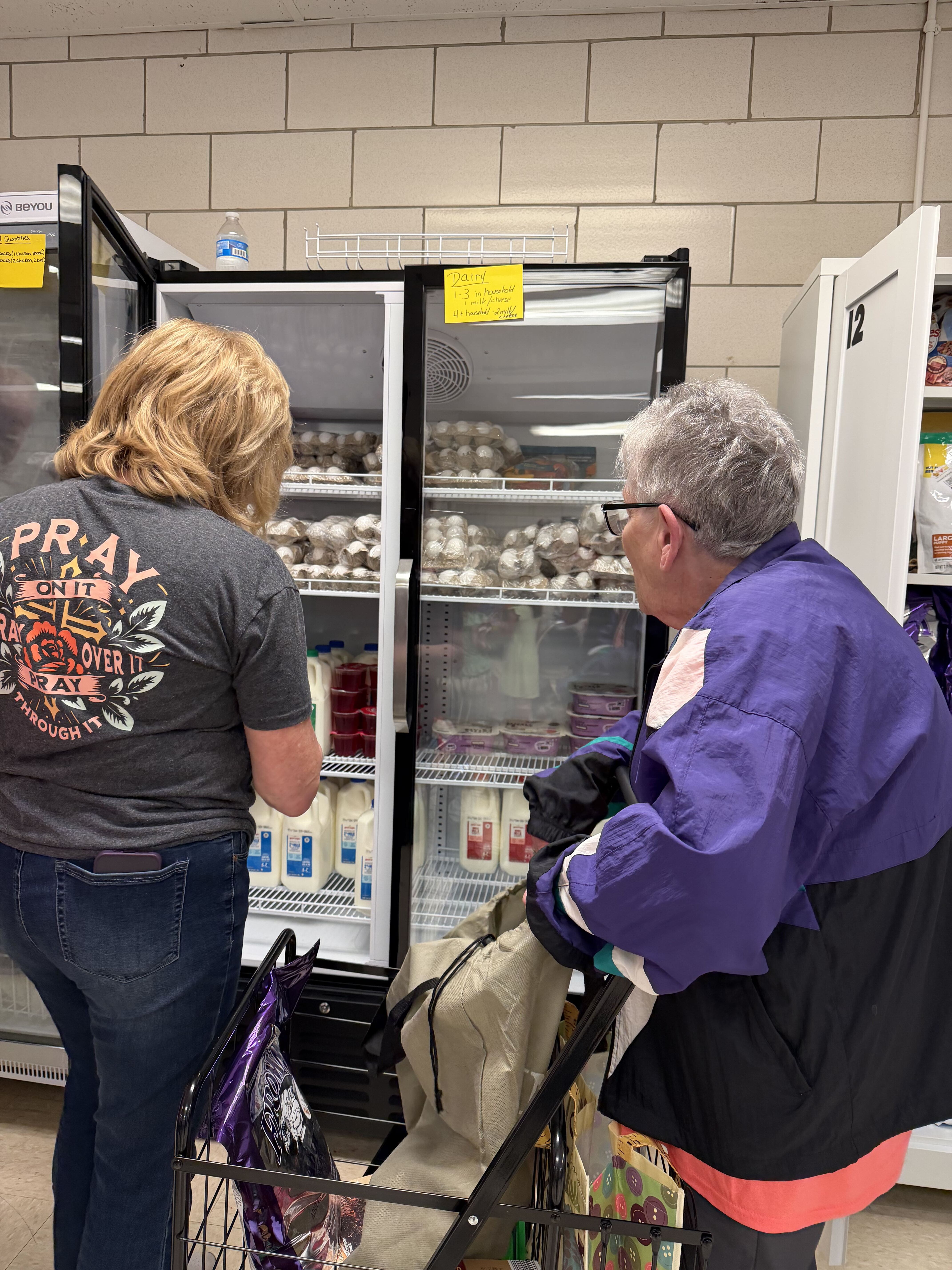 A volunteer helping a guest choose milk and eggs from the pantry fridge